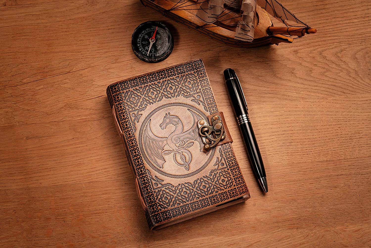 Small journal, leather handbound, placed on a table next to a pen, compass and model ship