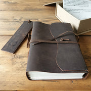 Rustic leather journal placed on wooden table, next to leather bookmark and protective box