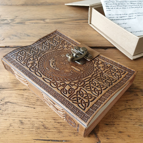 Tan leather notebook resting on wooden table alongside protective box