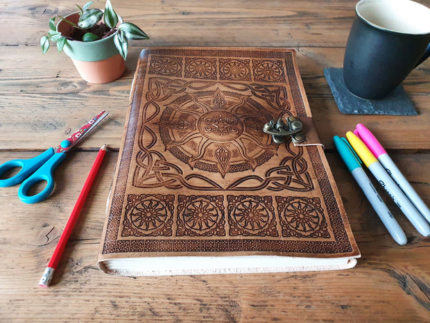 Large journal with Celtic sun design, on a table next to pens, scissors, a mug and a plant