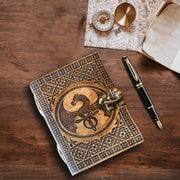 A6 travel journal embossed with Celtic dragon, placed on wooden table alongside a pen and explorer maps