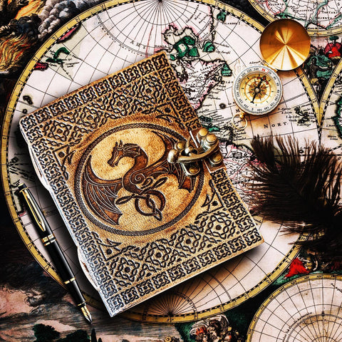 Explorers journal, embossed with dragon, resting on a table with explorer maps and compass